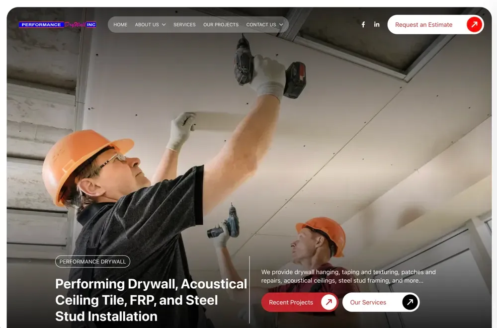 Worker in orange hard hat and gloves drilling into a ceiling panel, with a second worker beneath him.