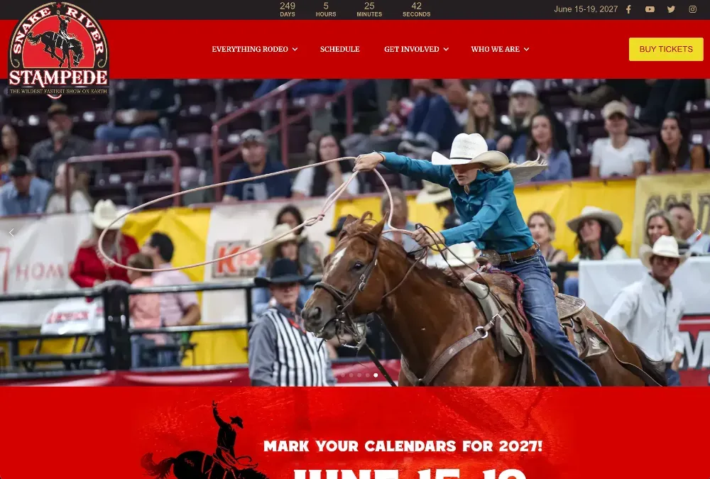 Rider in white hat and teal shirt roping on a galloping horse inside an arena, spectators watching from the stands.