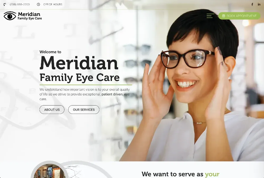 Smiling woman with short dark hair adjusting dark-framed glasses in an optical store with eyewear displayed behind her.